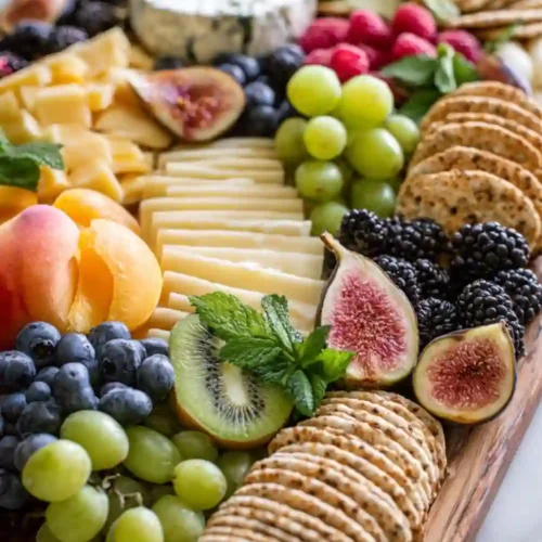 Holiday cheese and fruit board with assorted cheeses, figs, crackers, berries, grapes, kiwi, peaches, and fresh herbs arranged beautifully on a wooden board