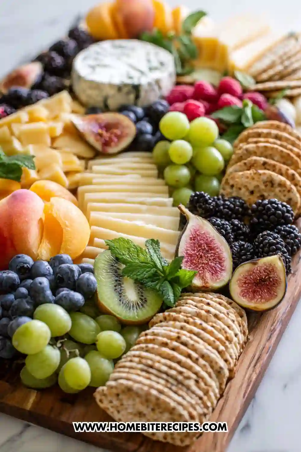 Holiday cheese and fruit board with assorted cheeses, figs, crackers, berries, grapes, kiwi, peaches, and fresh herbs arranged beautifully on a wooden board