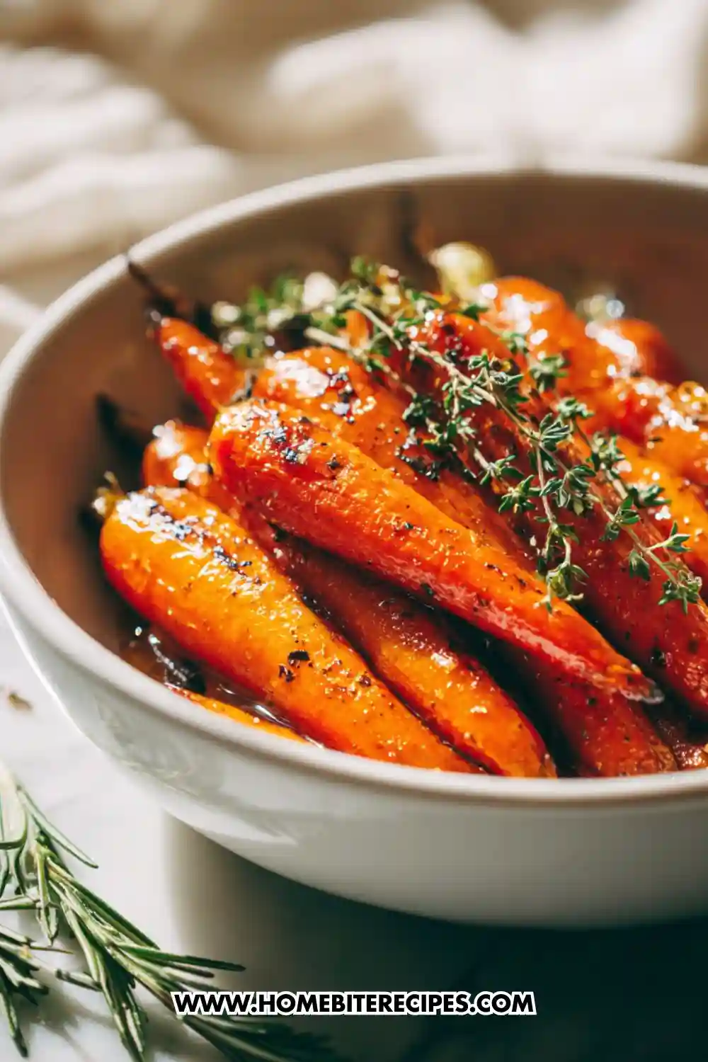 A bowl of glossy honey-garlic roasted carrots topped with fresh thyme and herbs, beautifully caramelized and served in a white dish.