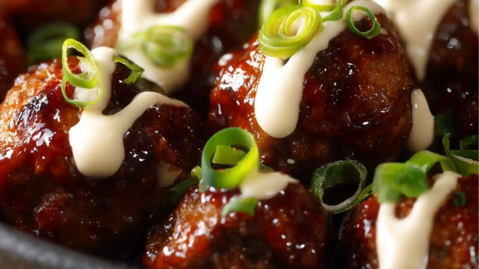 Close-up shot of Japanese spicy glazed meatballs topped with green onions, sesame seeds, and drizzled sauce, held with chopsticks.