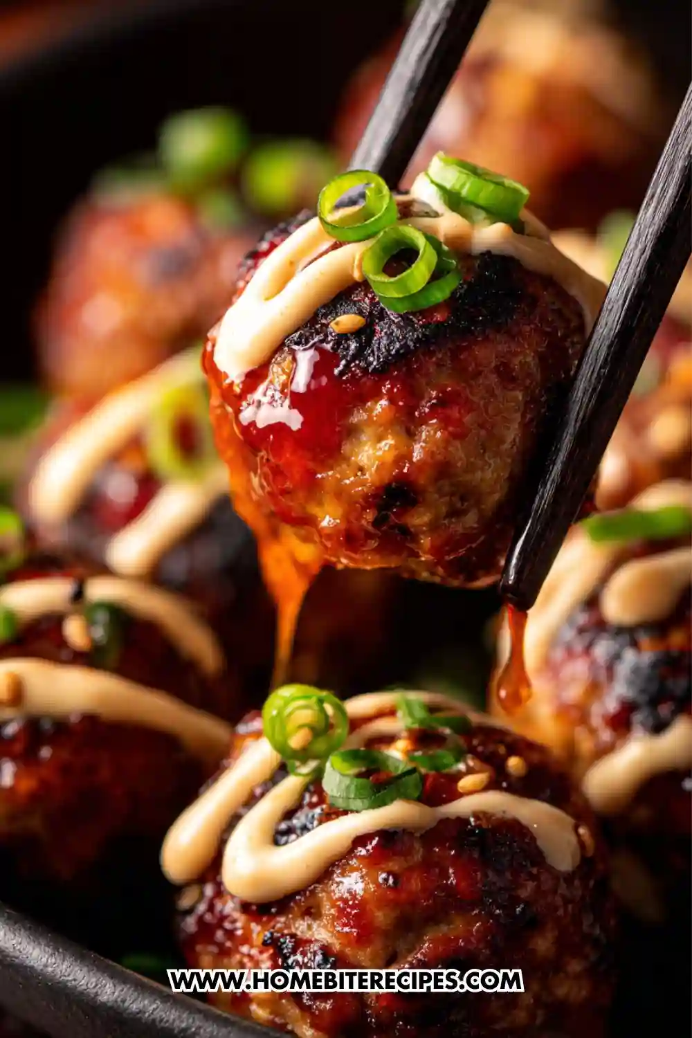 Close-up shot of Japanese spicy glazed meatballs topped with green onions, sesame seeds, and drizzled sauce, held with chopsticks.