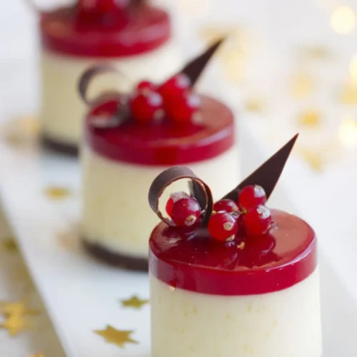 Mini white chocolate mousse cakes with red berry glaze and chocolate decorations, served on a white plate with gold stars.