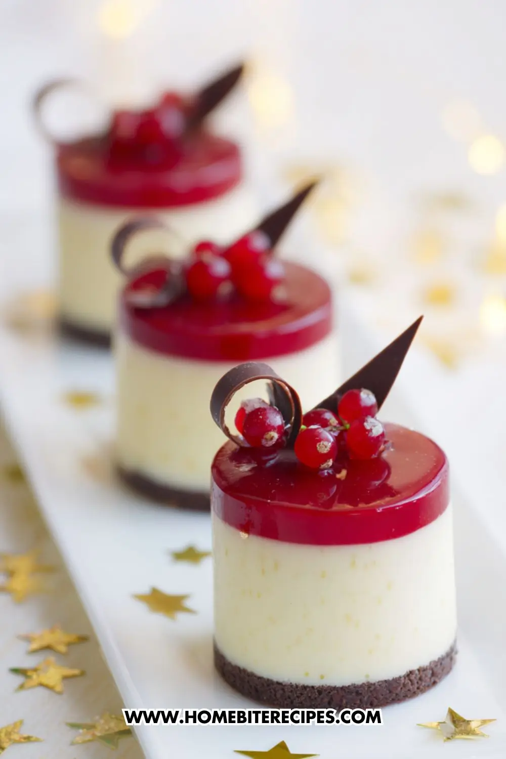 Mini white chocolate mousse cakes with red berry glaze and chocolate decorations, served on a white plate with gold stars.