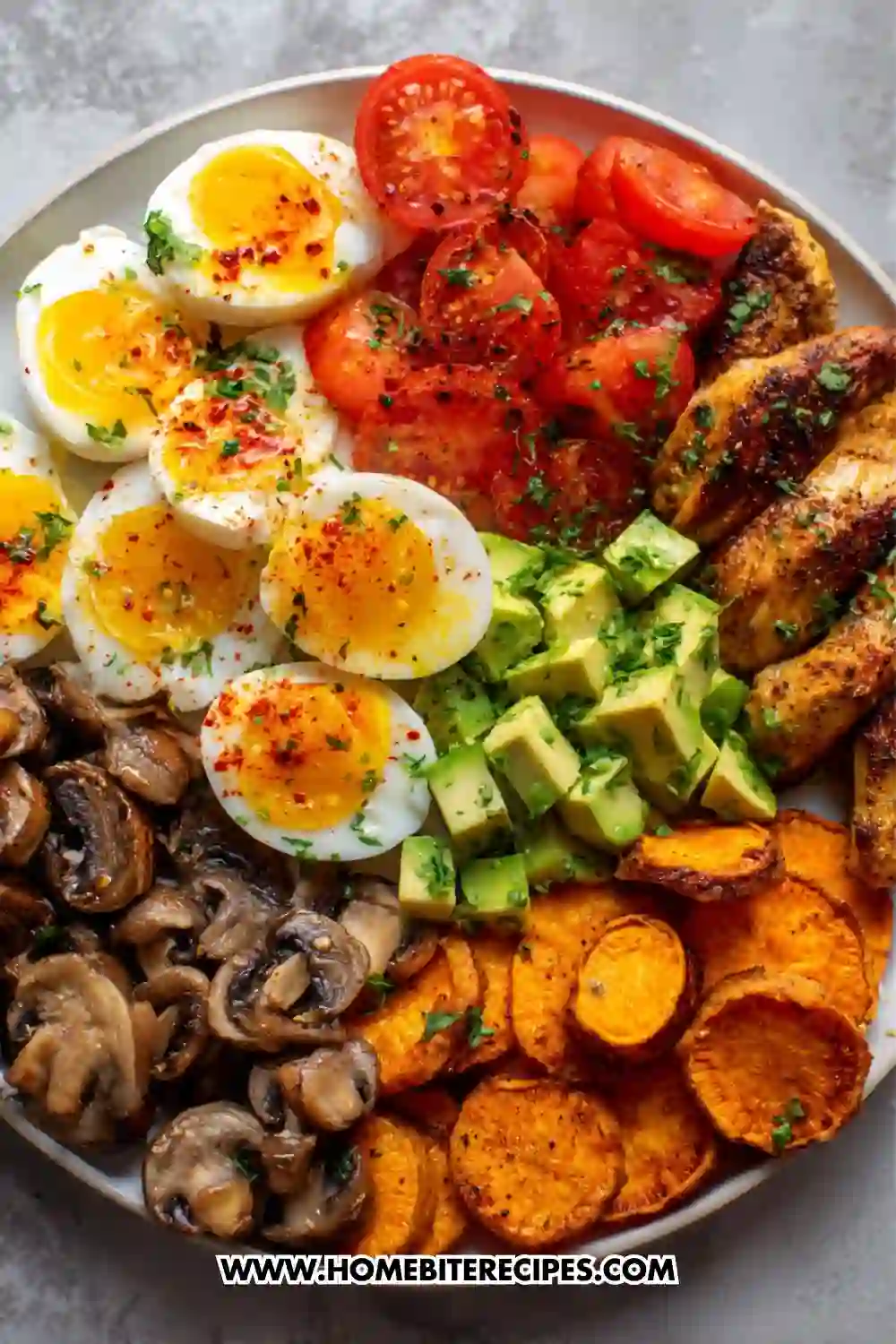 A colorful and nutritious breakfast bowl filled with soft-boiled eggs, seasoned chicken strips, avocado cubes, roasted sweet potatoes, sautéed mushrooms, and fresh tomato slices arranged beautifully on a plate.