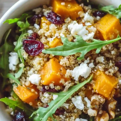 Colorful quinoa salad with roasted butternut squash, arugula, walnuts, cranberries, and goat cheese served in a white bowl — a healthy and vibrant fall meal