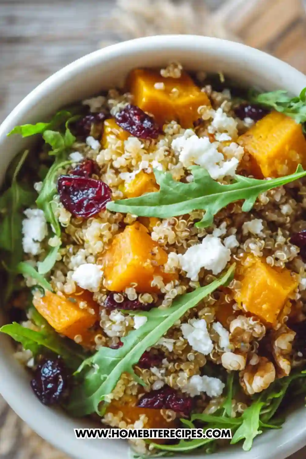 Colorful quinoa salad with roasted butternut squash, arugula, walnuts, cranberries, and goat cheese served in a white bowl — a healthy and vibrant fall meal