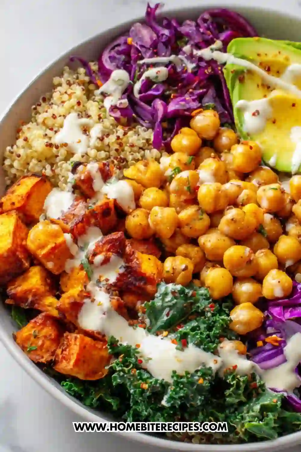 A vibrant vegan Buddha bowl filled with roasted sweet potatoes, chickpeas, quinoa, avocado, kale, and purple cabbage drizzled with creamy tahini dressing.