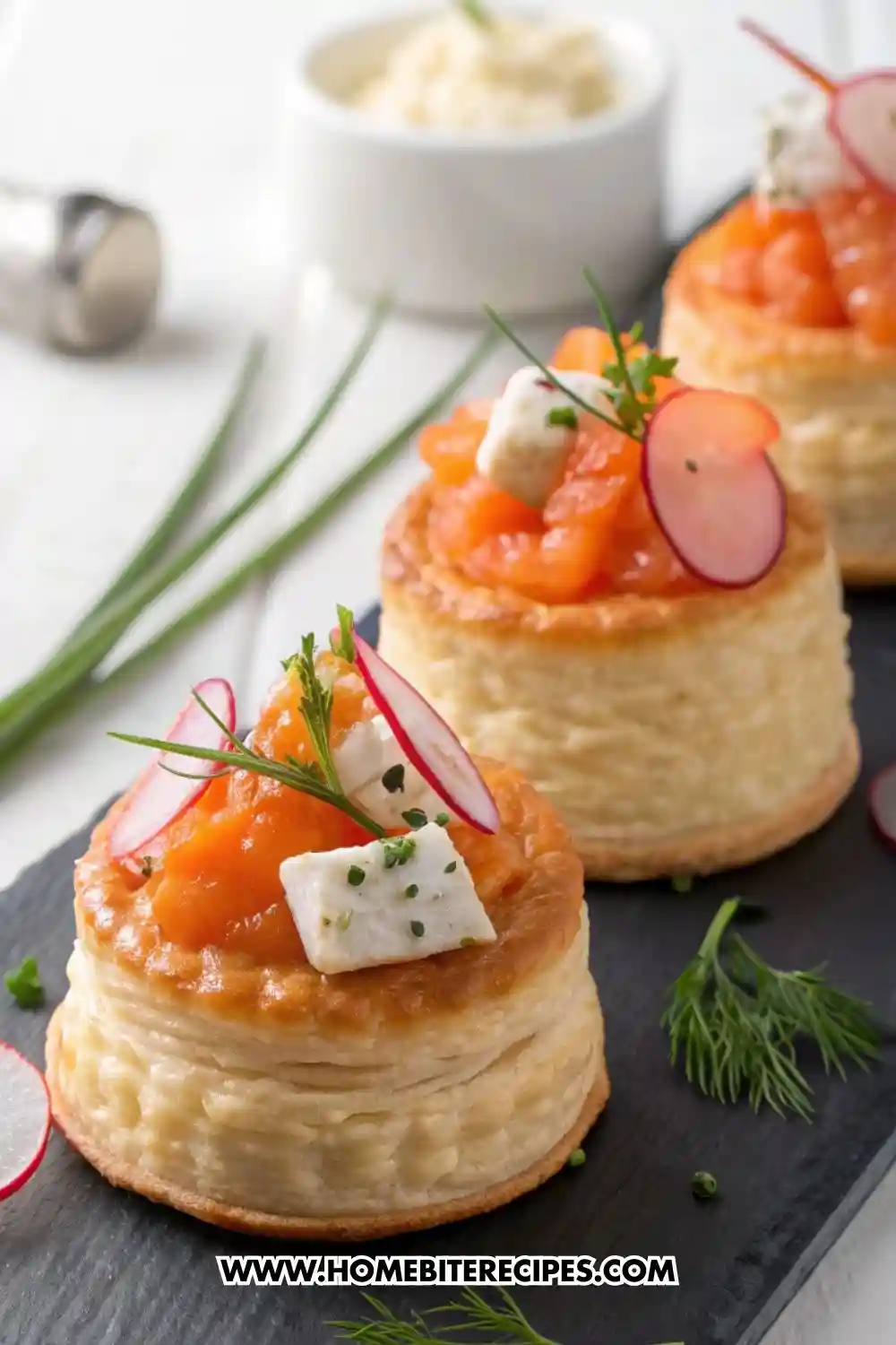 Elegant puff pastry vol-au-vent filled with smoked salmon, cream cheese, radish slices, and fresh herbs, served on a black slate board.