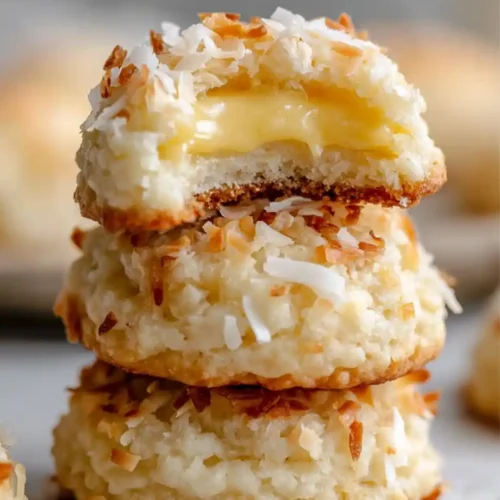 Close-up image of soft coconut macaroons stacked, filled with creamy lemon custard and topped with toasted coconut flakes.