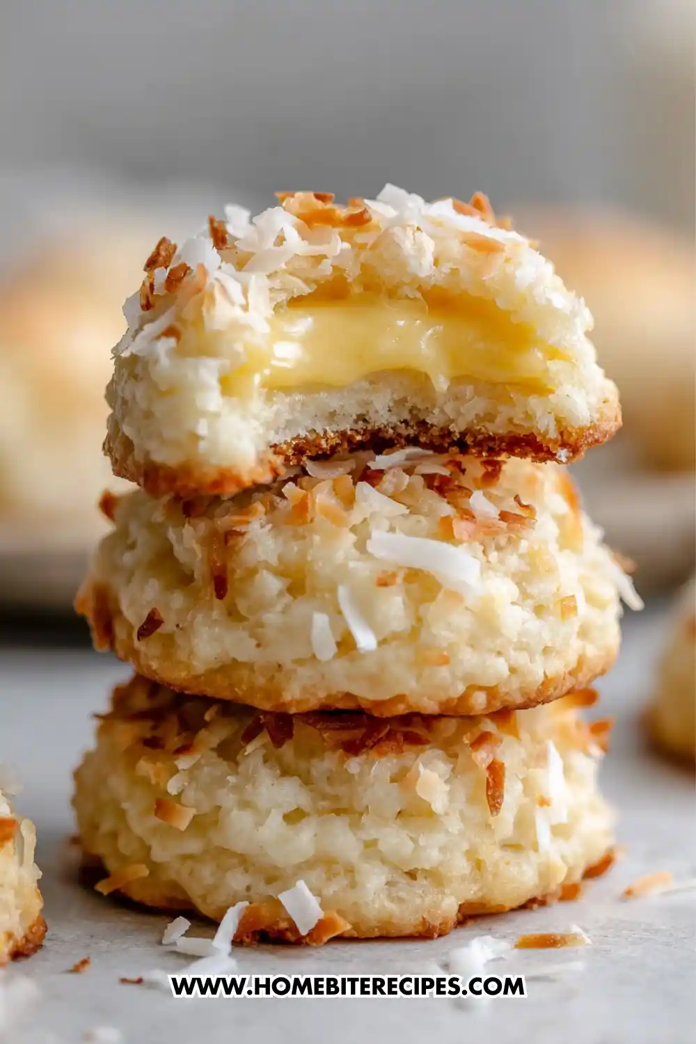 Close-up image of soft coconut macaroons stacked, filled with creamy lemon custard and topped with toasted coconut flakes.