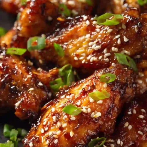 Close-up of sticky honey garlic chicken wings sprinkled with sesame seeds and green onions, perfectly glazed and golden brown.