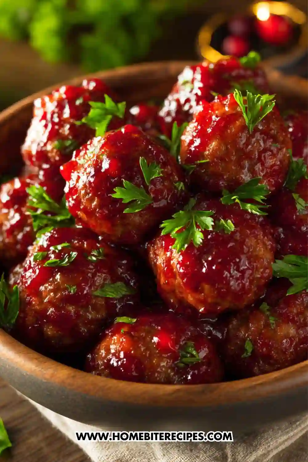 Close-up image of juicy meatballs coated in a glossy cranberry glaze, garnished with fresh parsley in a wooden bowl.