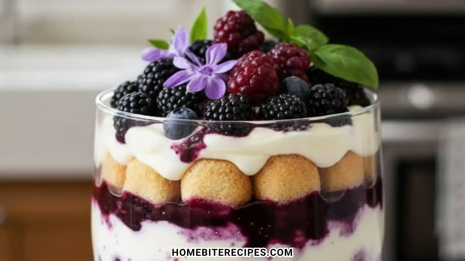 A close up layered Berry Tiramisu Trifle in a glass bowl featuring ladyfingers, creamy mascarpone, and mixed berry compote topped with fresh blackberries and raspberries.