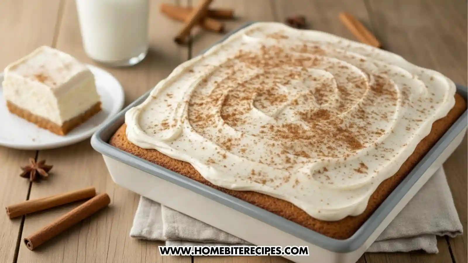 A full view of a square Chai Spiced Layer Cake in a baking pan, topped with a thick swirl of white frosting and a generous dusting of cinnamon spice.