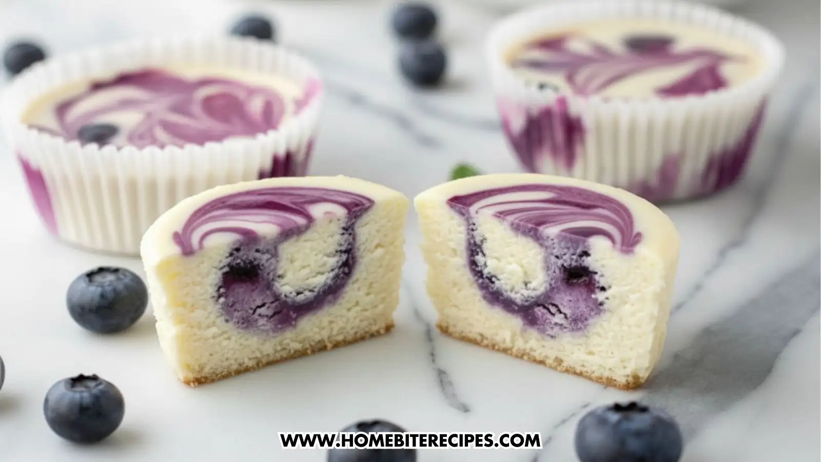 Mini blueberry swirl cheesecake cups in white muffin liners on a marble surface, topped with purple blueberry puree swirls and fresh whole blueberries around them, one of these muffin is cutted in half to show the lovely blueberry swirl