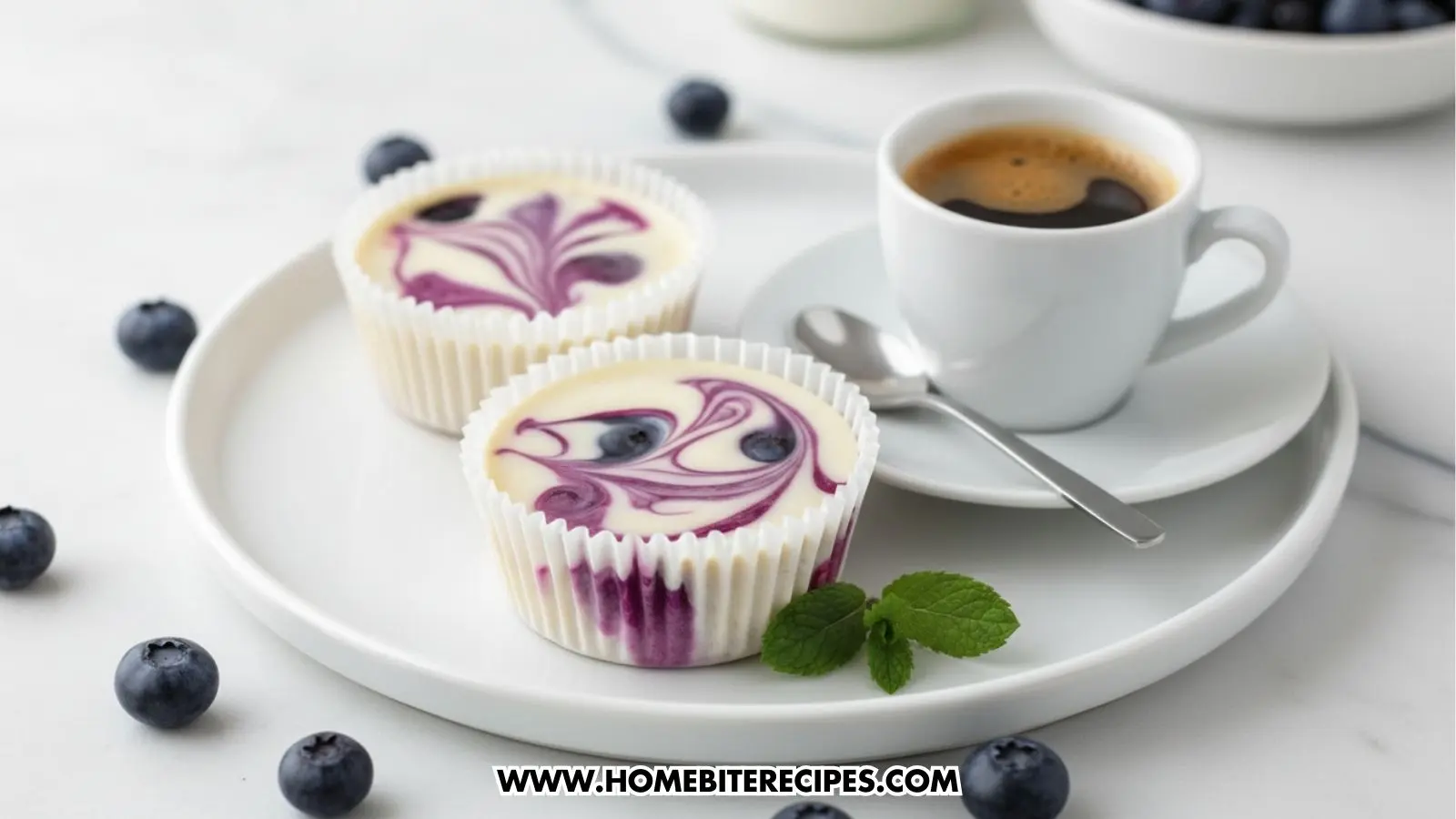 Two mini Blueberry Swirl Cheesecake Cups in white muffin liners served with a fresh cup of coffee on a white plate