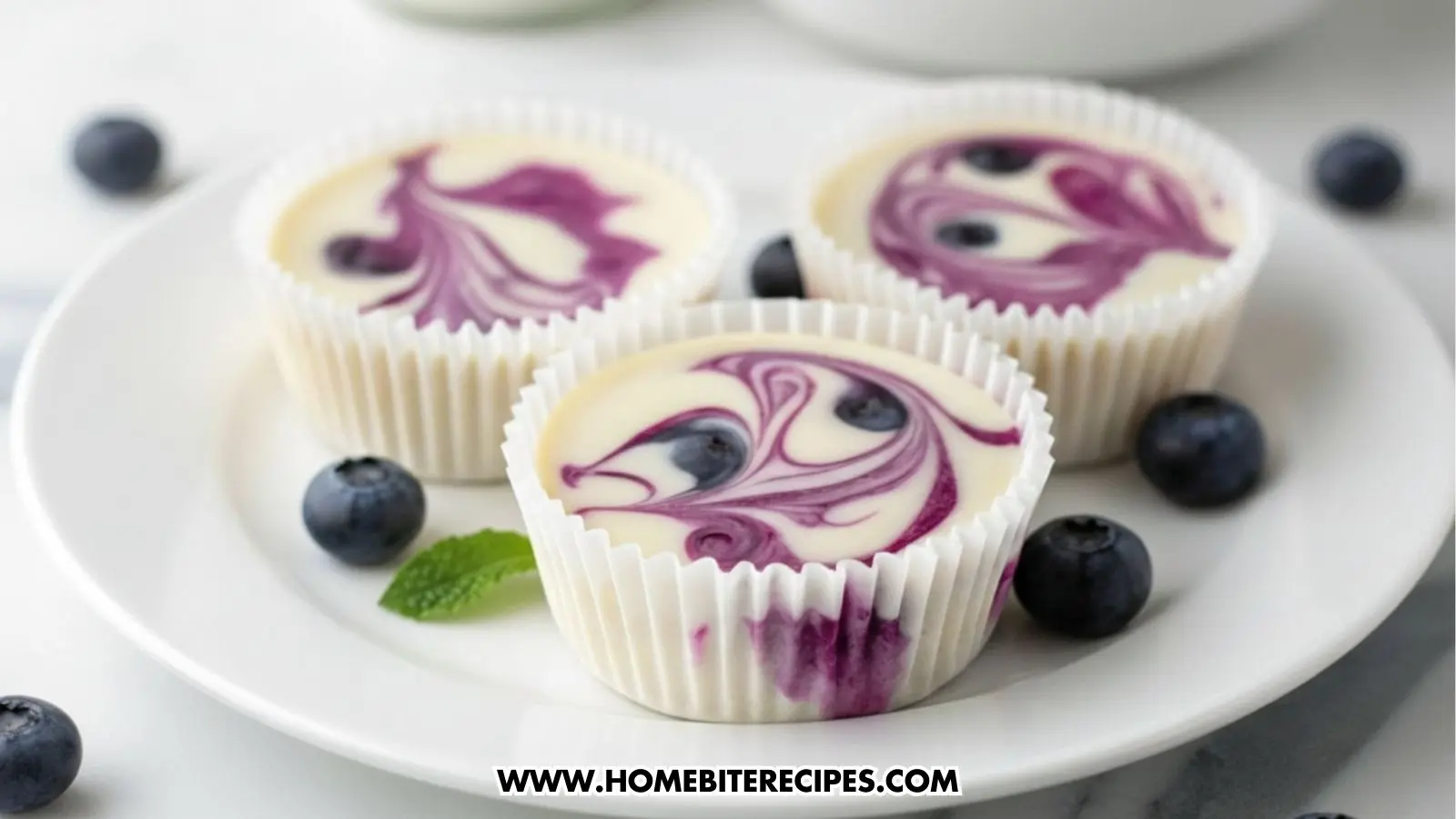 Mini blueberry swirl cheesecake cups in white muffin liners on a marble surface, topped with purple blueberry puree swirls and fresh whole blueberries around them.