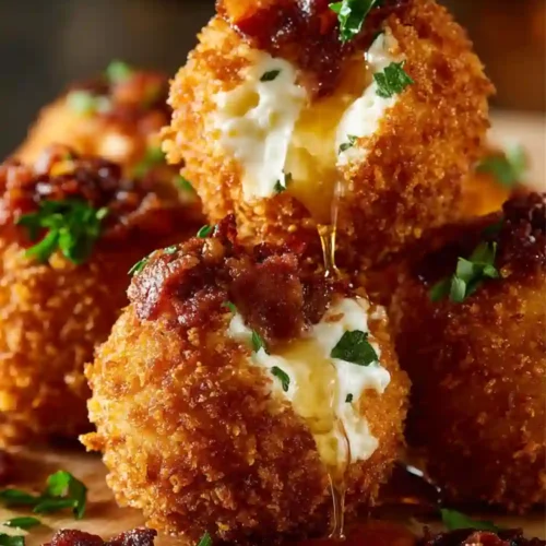 Close-up of crispy buffalo chicken mozzarella bombs filled with melted cheese, topped with bacon and herbs, dripping with sauce.
