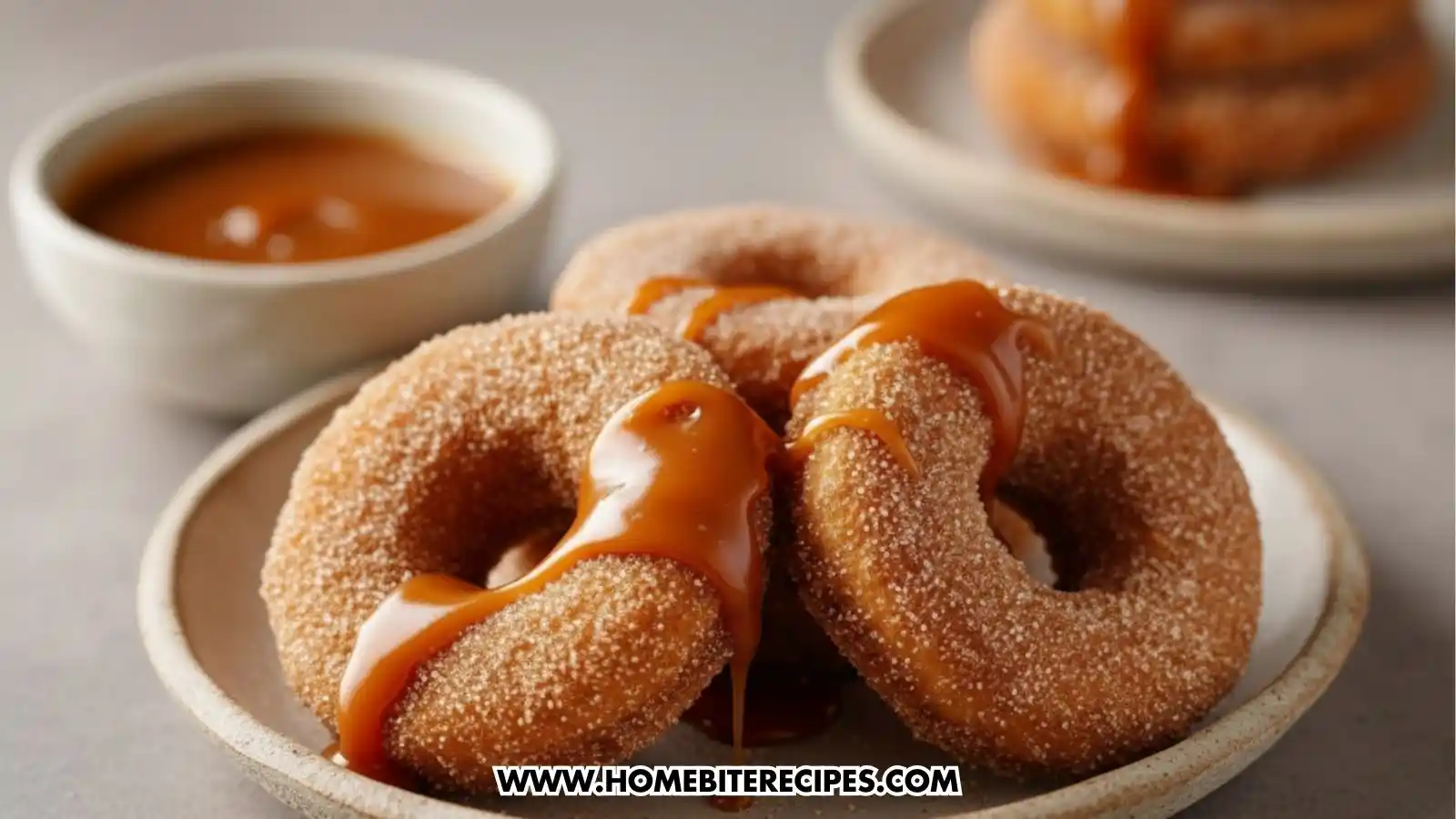 Cinnamon sugar donuts covered in warm dripping caramel sauce on a white plate and a bowl of caramel on the background