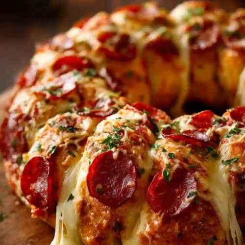A golden pull-apart bread wreath loaded with melted mozzarella, beef pepperoni slices, garlic butter, and fresh herbs, with cheese stretching between the pieces.
