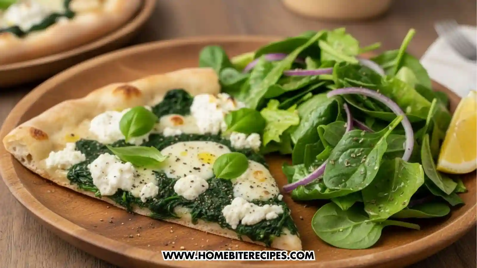 A thin-crust pizza slice topped with a layer of sautéed spinach, large dollops of white cheese, and fresh basil leaves, seasoned with cracked black pepper. It is served on a wooden plate alongside a fresh green side salad with red onions and a lemon wedge.
