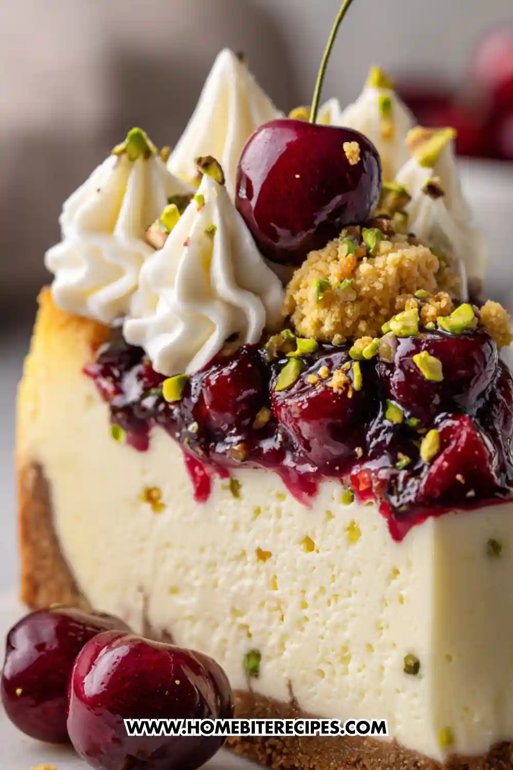 Slice of creamy cheesecake topped with glossy cherries, piped whipped cream, pistachios, and crumbled topping on a graham crust.