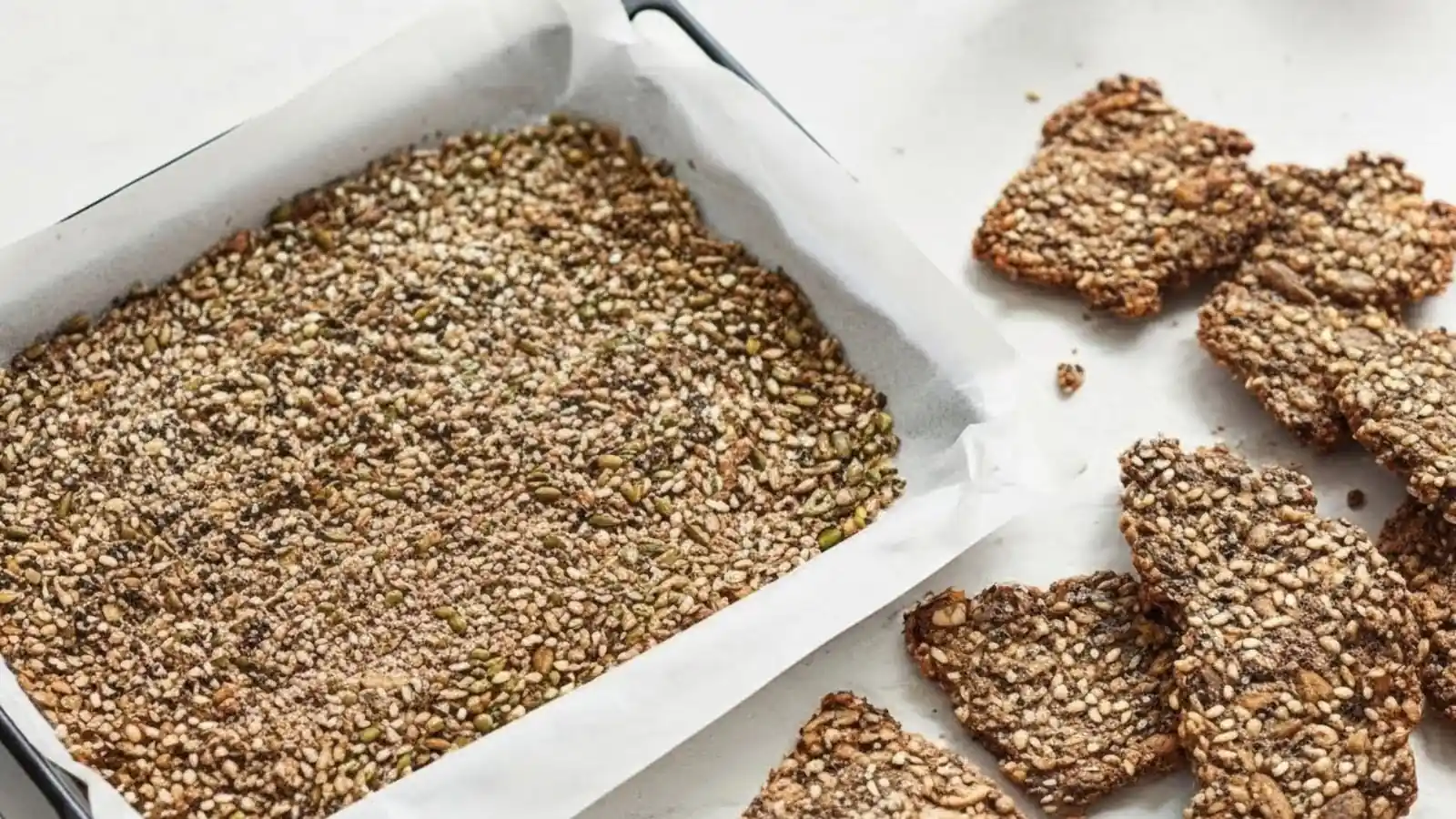 Homemade Chia Flax Seed Crackers being baked on a parchment-lined tray next to finished, crispy seed crackers.