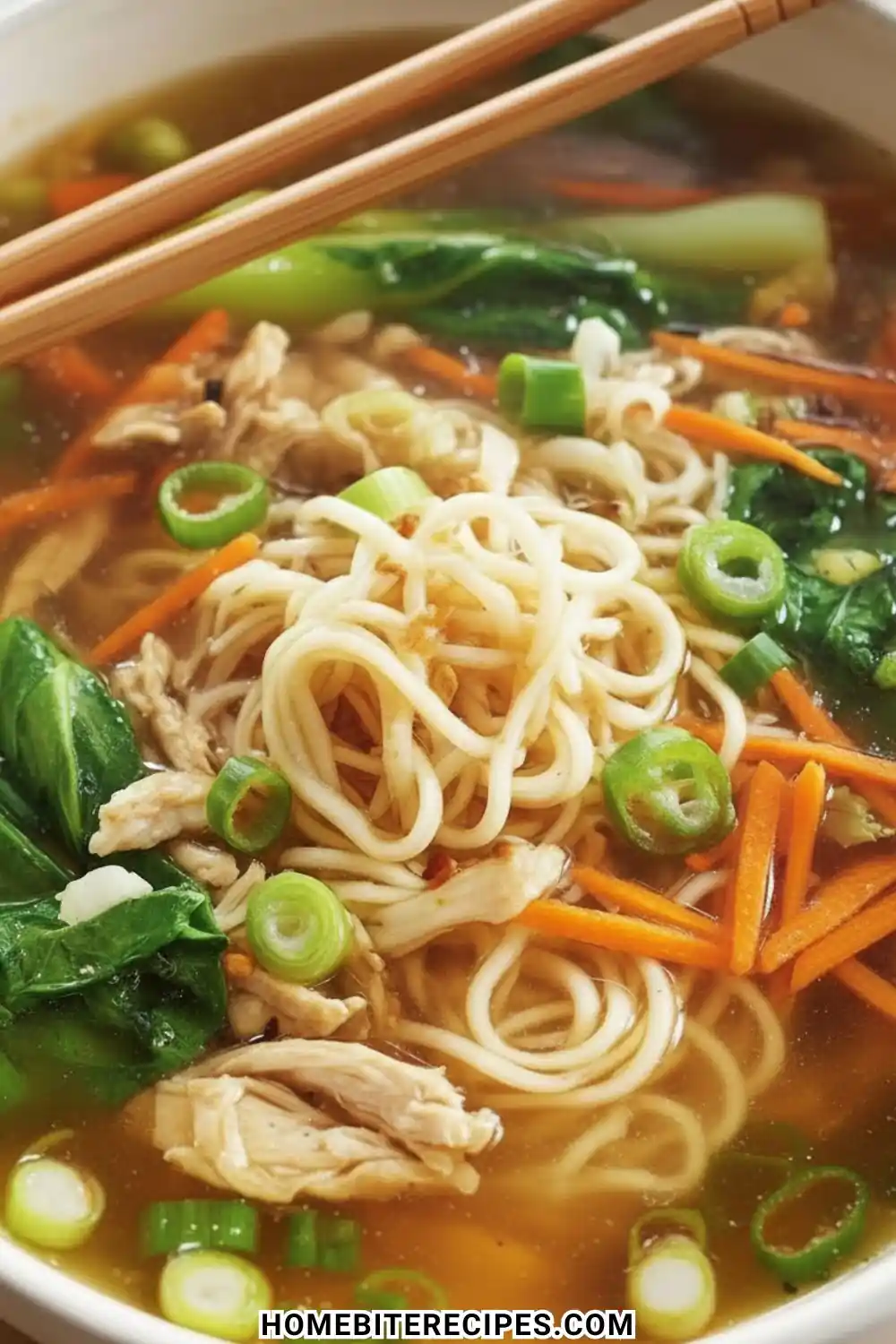 A close-up bowl of Chicken Noodle Soup with Ginger Scallion featuring ramen noodles, shredded chicken, sliced carrots, and fresh bok choy.