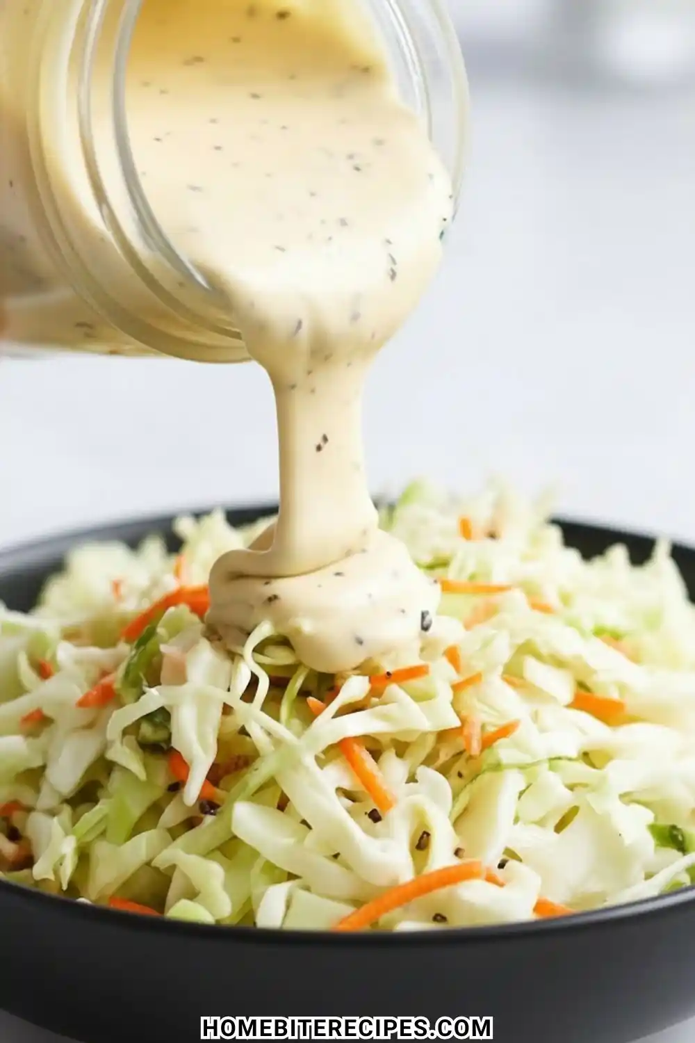 Creamy Classic Homemade Coleslaw Dressing being poured from a glass jar onto a fresh bowl of shredded cabbage and carrots.