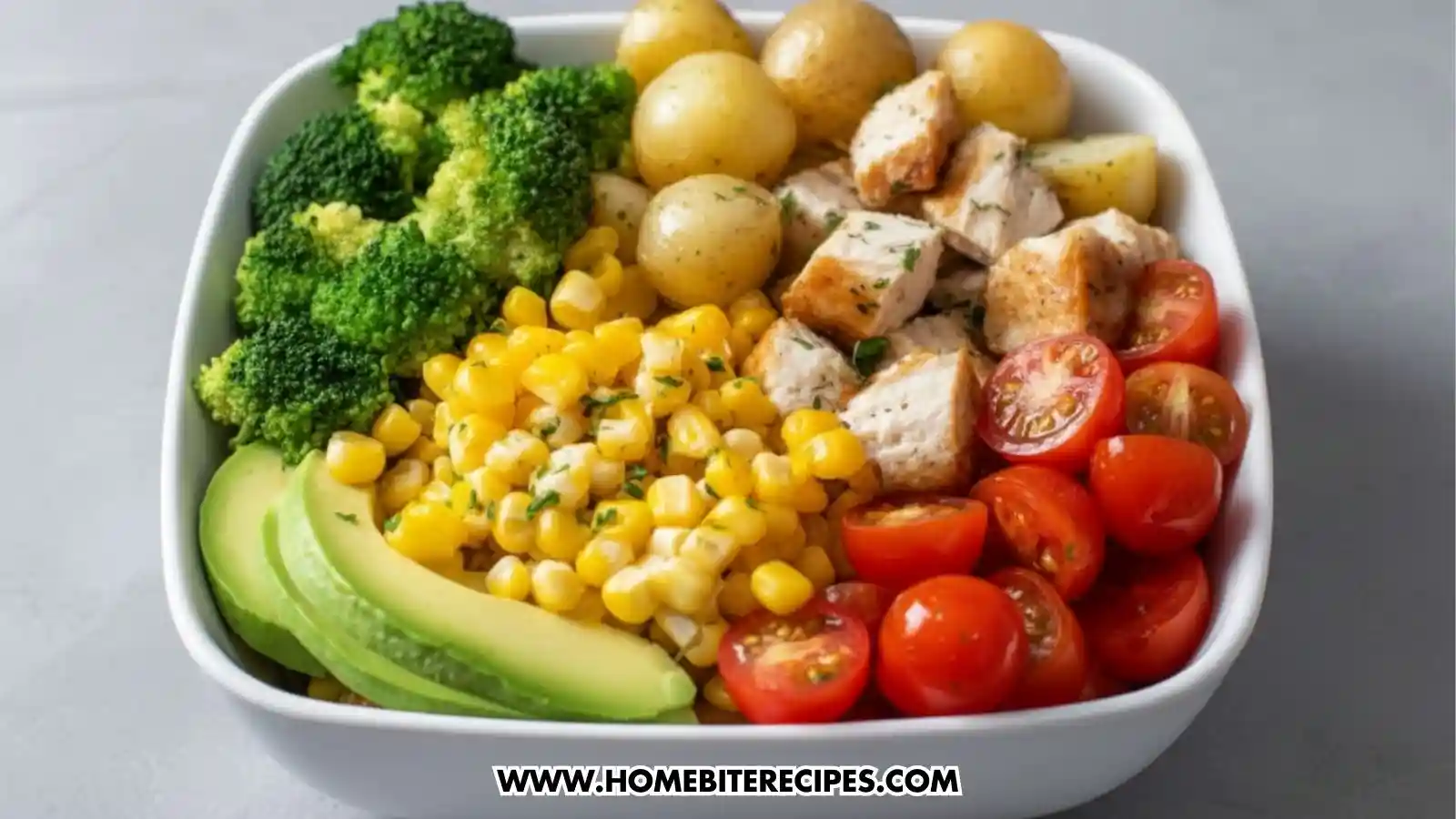 Clean eating chicken bowl with grilled chicken, baby potatoes, broccoli, corn, avocado slices, and cherry tomatoes.