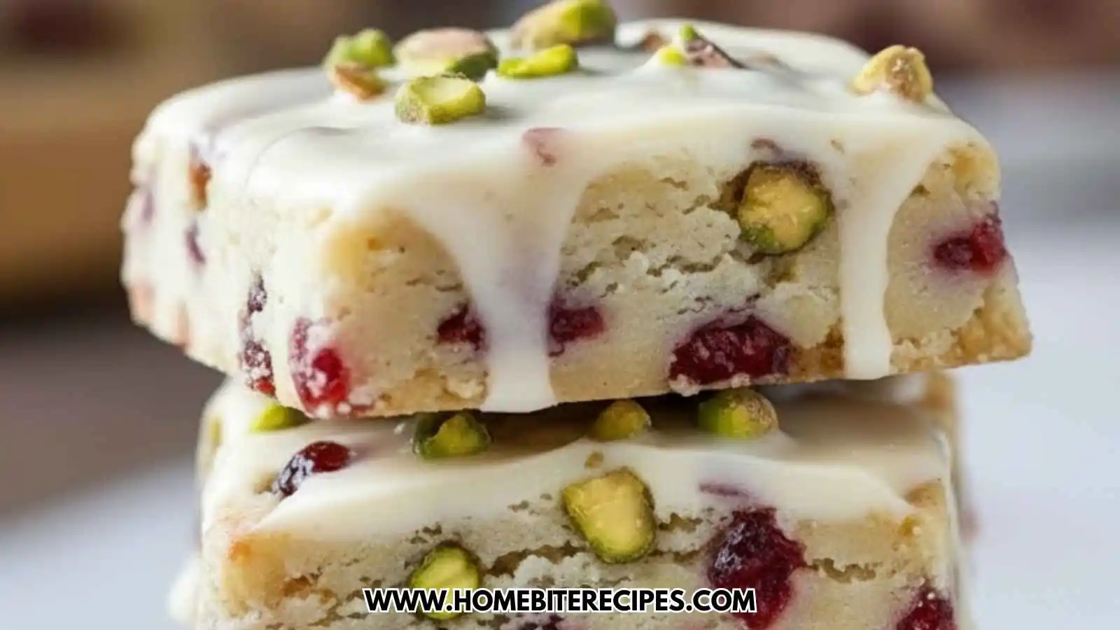 A close up stack of Cranberry Pistachio Shortbread Cookies featuring a white chocolate glaze, dried cranberries, and chopped green pistachios.