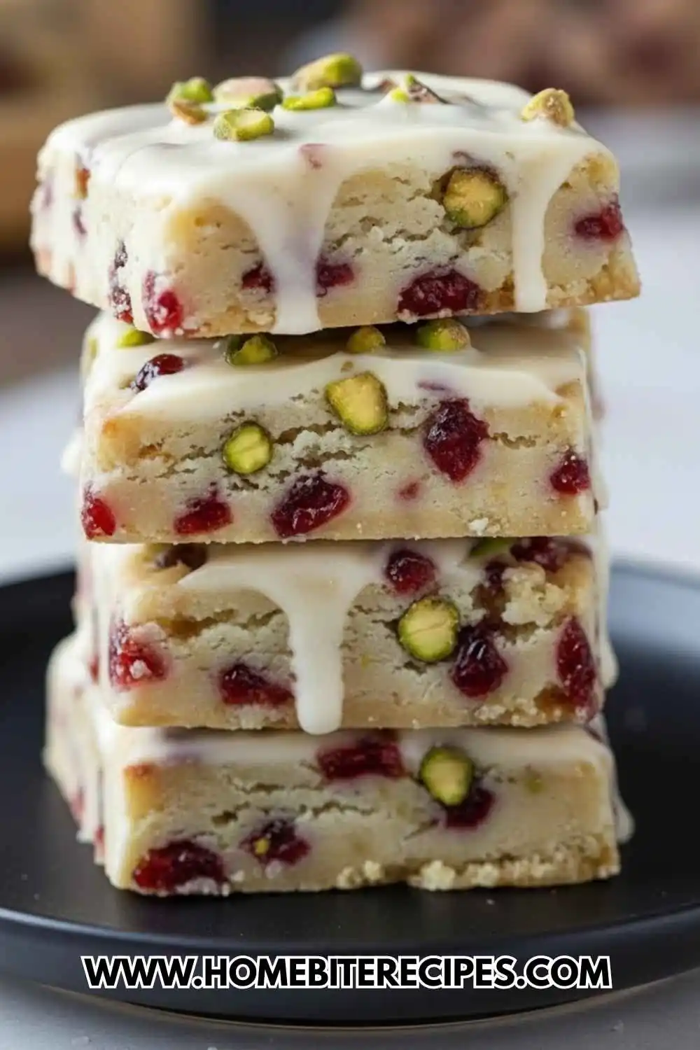 A tall stack of four square Cranberry Pistachio Shortbread Cookies featuring a white chocolate glaze, dried cranberries, and chopped green pistachios.