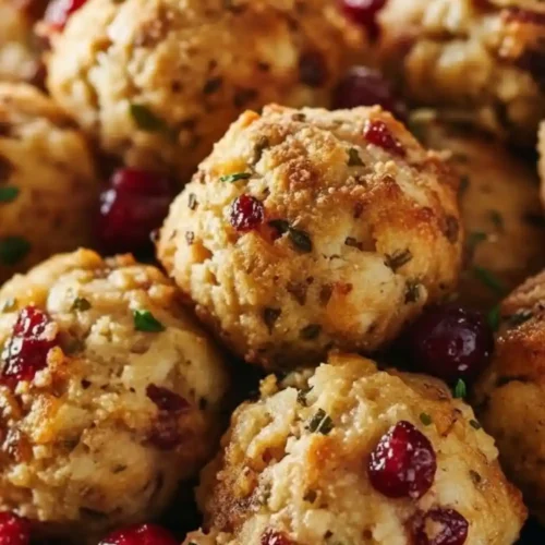 Golden-brown Cranberry Turkey Stuffing Balls garnished with fresh herbs and whole red cranberries on a dark plate