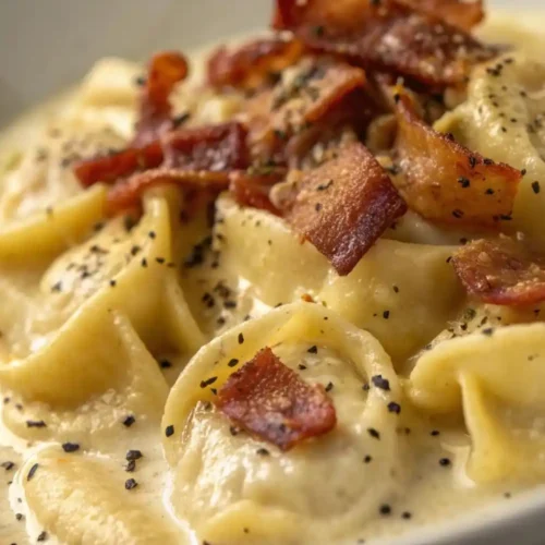 Creamy cheese tortellini Alfredo pasta topped with crispy bacon and black pepper in a white bowl.