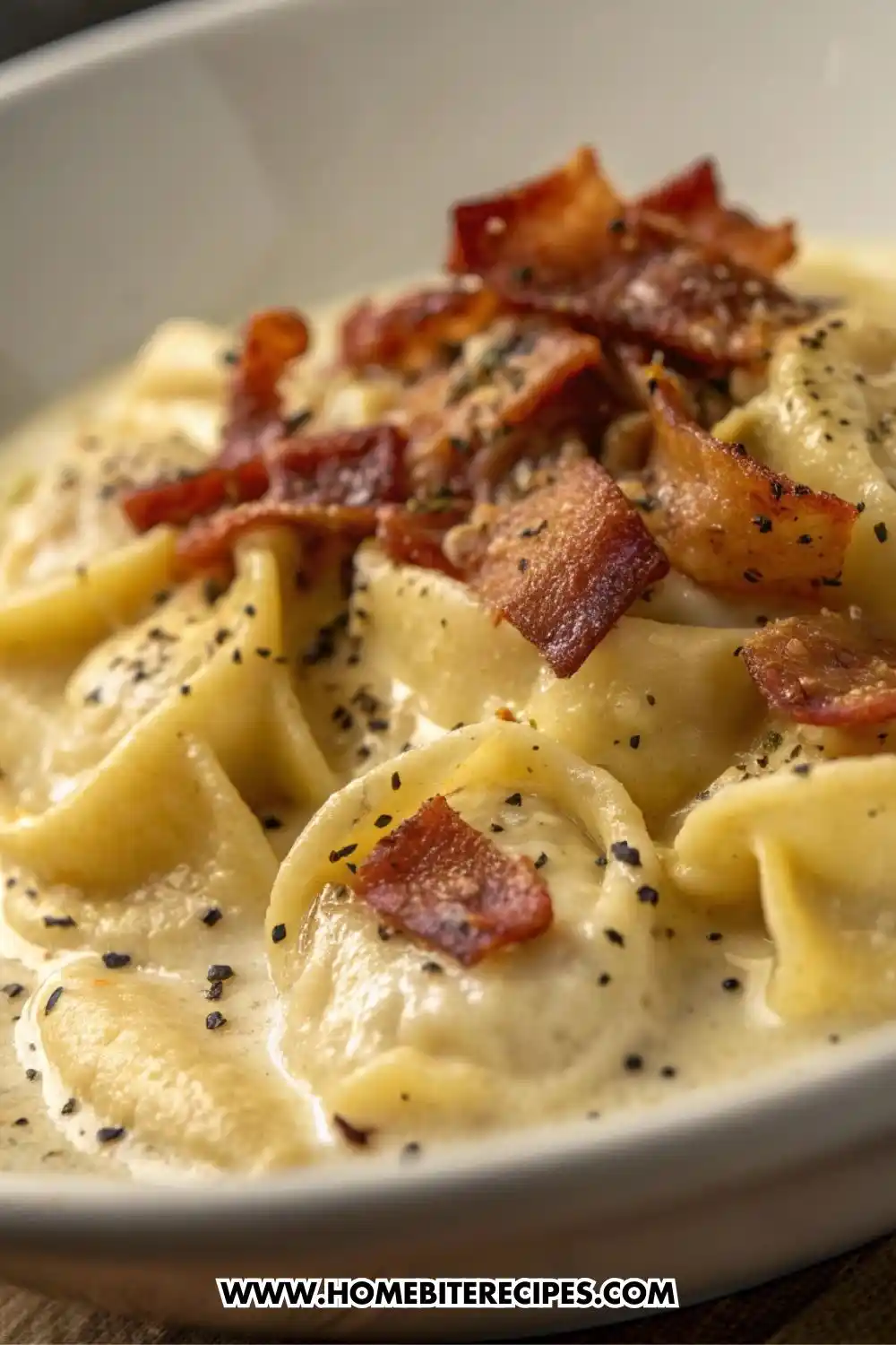Creamy cheese tortellini Alfredo pasta topped with crispy bacon and black pepper in a white bowl.