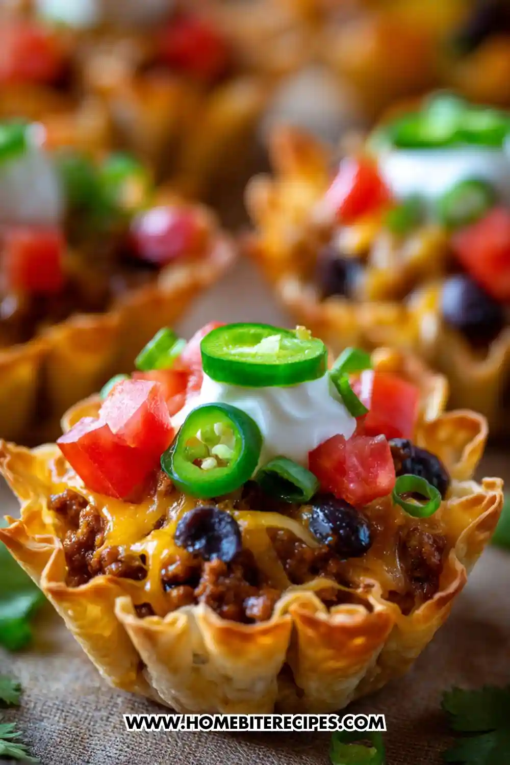 Close-up image of crispy air fryer taco phyllo cups filled with seasoned beef, melted cheese, black beans, and topped with sour cream, diced tomatoes, jalapeños, and green onions.