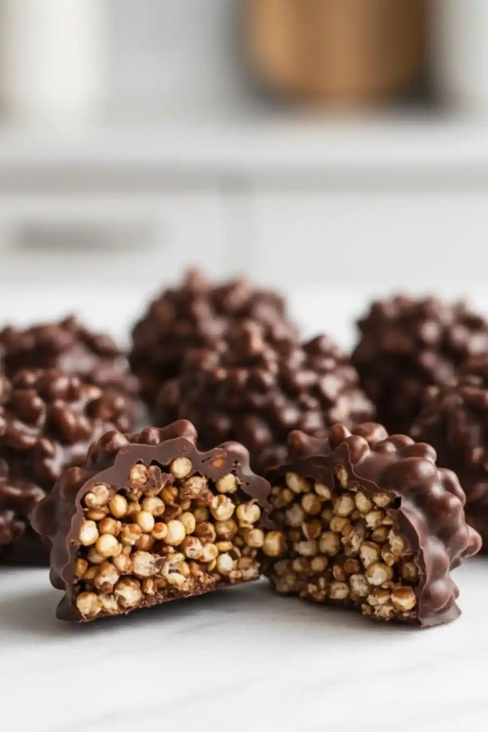 Close-up of dark chocolate quinoa crisps with one crisp broken open, showing crunchy puffed quinoa coated in rich dark chocolate.