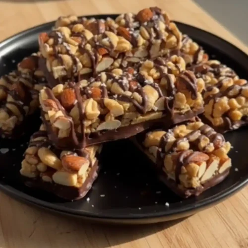 A stack of homemade Dark Chocolate Sea Salt Nut Bars drizzled with chocolate on a black plate, showcasing peanuts and almonds