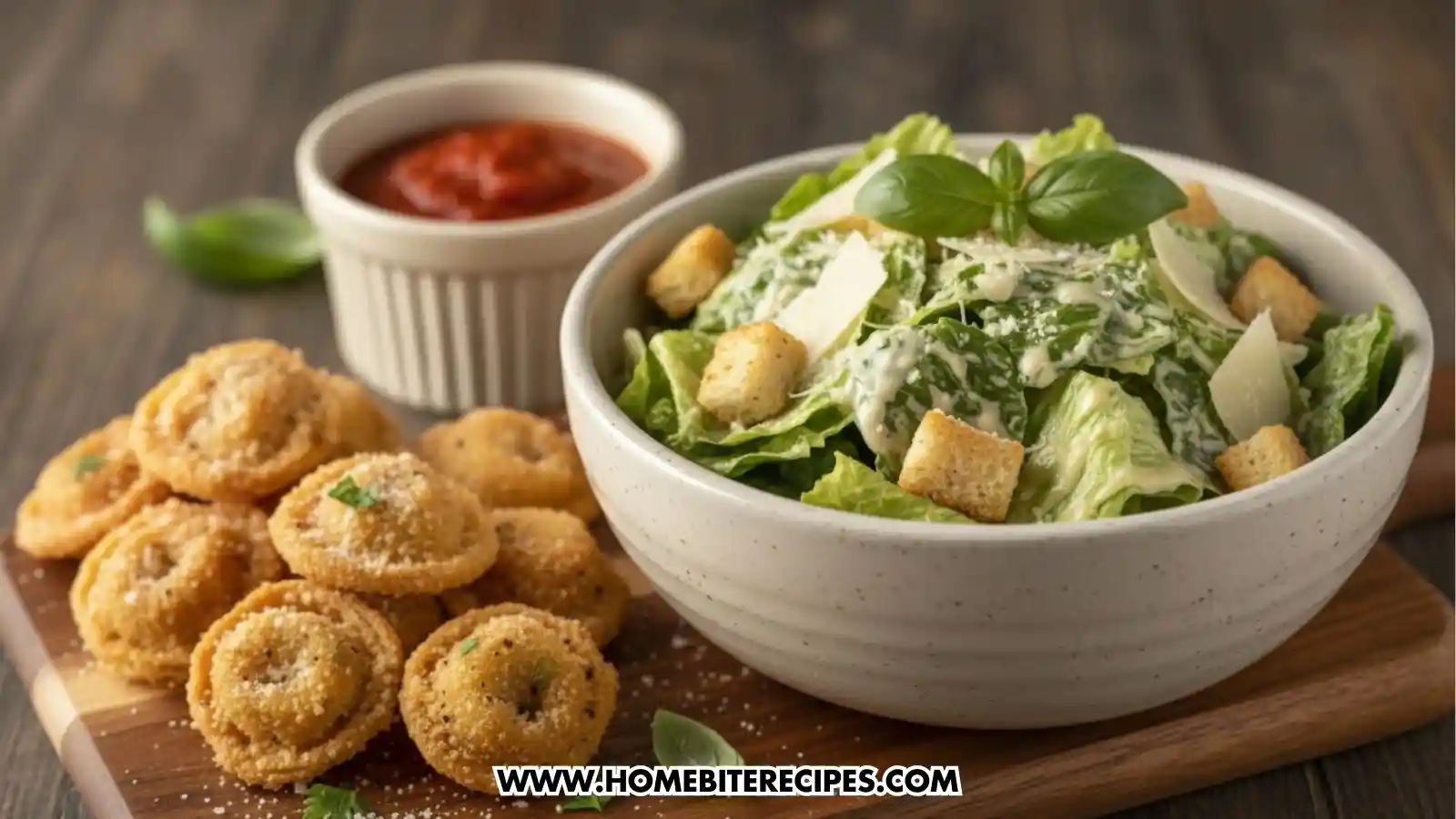 A wooden serving board featuring a pile of crispy, golden fried tortellini sprinkled with parmesan cheese on the left. Beside it is a large white bowl of Caesar salad with romaine lettuce, large croutons, and shaved parmesan. A small container of red dipping sauce sits in the background.