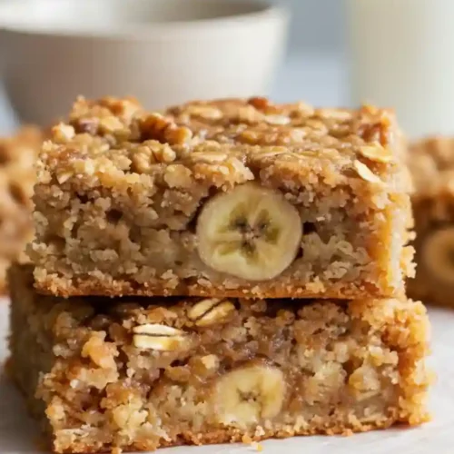 A stack of two moist Banana Oatmeal Bars on a cutting board, clearly showing a slice of banana baked into the center of each bar.