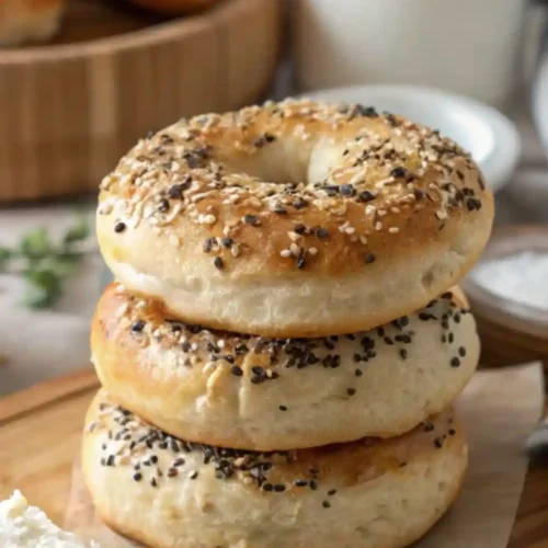Stack of fluffy homemade cottage cheese almond flour bagels topped with everything seasoning, served on a wooden board.