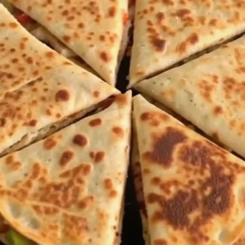 Crispy chicken and vegetable quesadilla wedges cooked until golden brown and sliced into triangles on a black pan.
