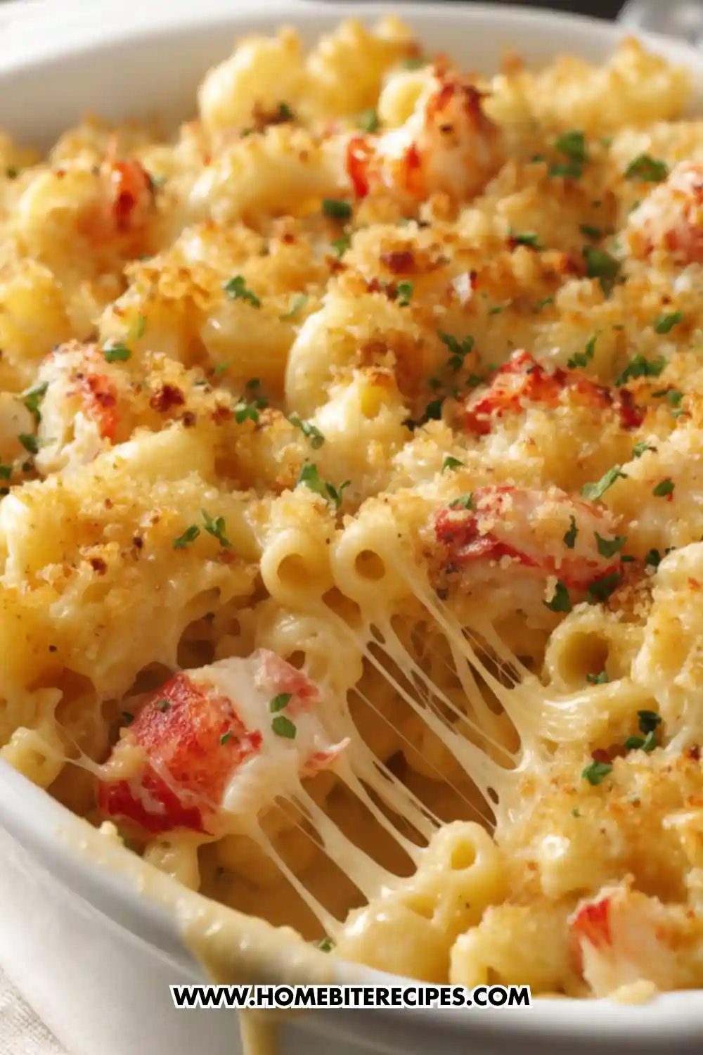 Close-up of creamy lobster mac and cheese in a white baking dish, topped with golden crispy breadcrumbs, fresh parsley, and stretchy melted cheese.