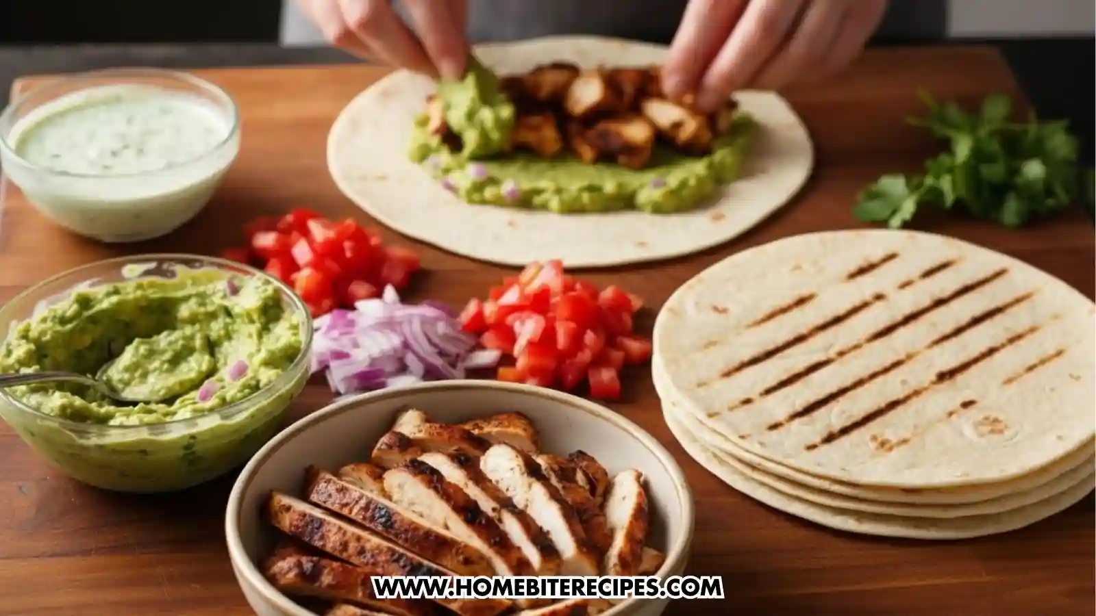 A person is assembling a grilled chicken guacamole wrap on a wooden cutting board, surrounded by bowls of sliced grilled chicken, guacamole, a creamy white sauce, diced tomatoes, chopped red onions, and a stack of grilled flour tortillas.
