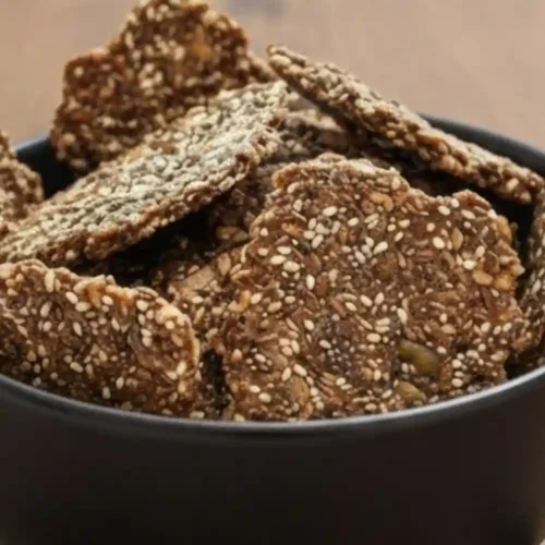 A bowl of crispy, homemade Chia Flax Seed Crackers showing a rich texture of sesame, chia, and flax seeds.