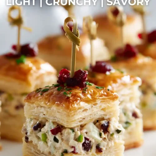 Close-up of healthy chicken puff pastry bites filled with creamy chicken salad, topped with herbs and cranberries, served as a bite-sized party appetizer