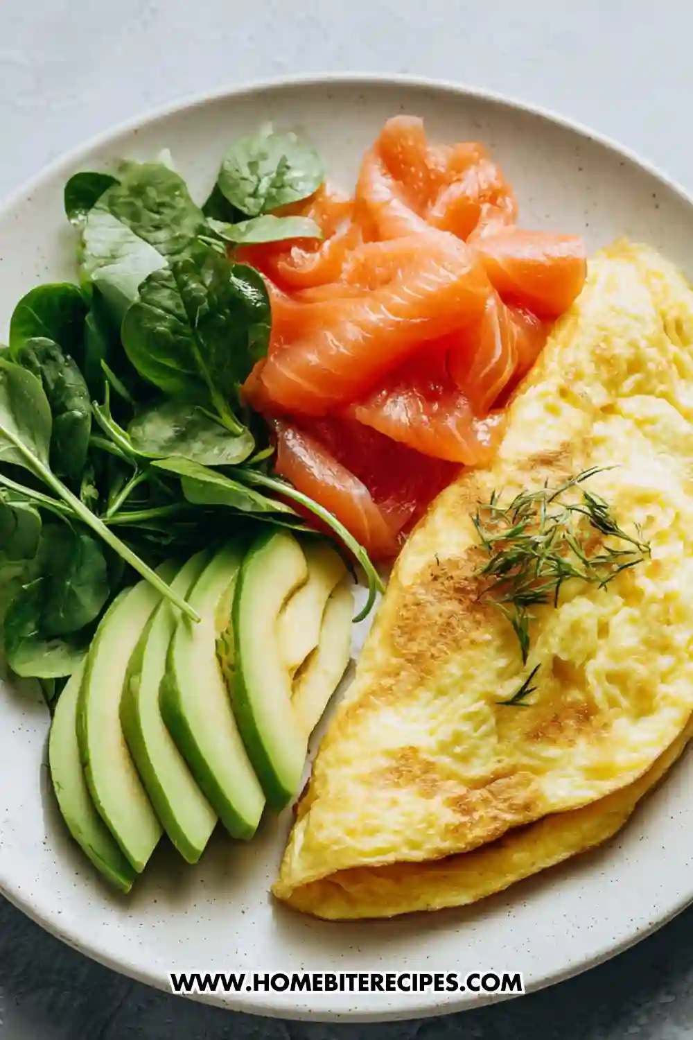 Healthy omelet served with smoked salmon, sliced avocado, and fresh spinach on a ceramic plate, topped with dill and prepared as a low-carb breakfast.
