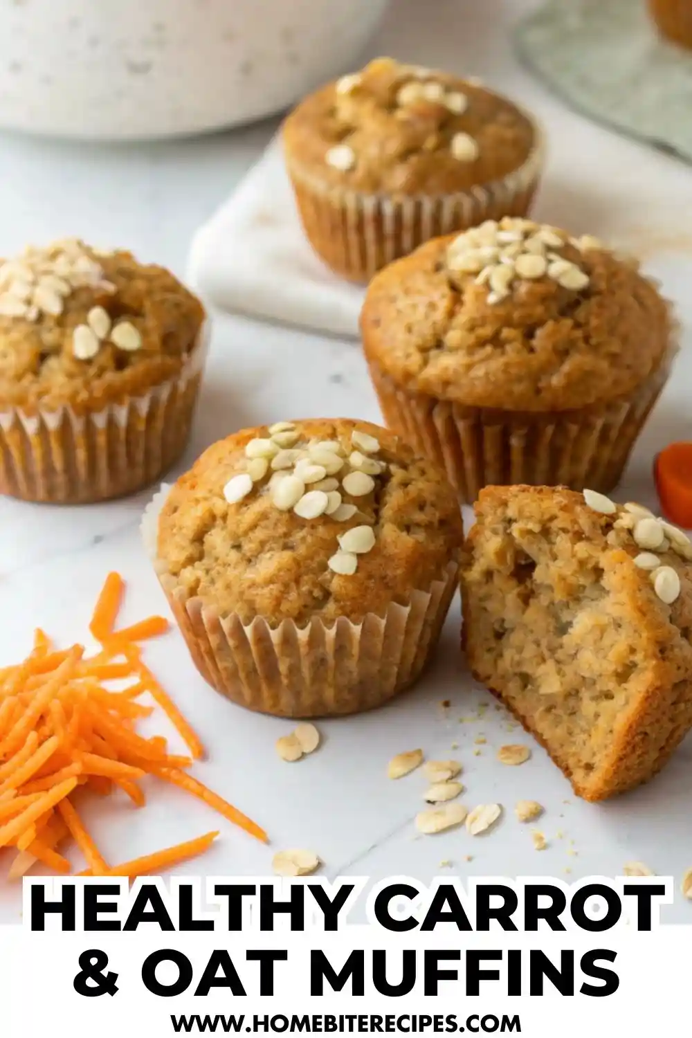 Close-up photo of freshly baked healthy carrot and oat muffins topped with oats, arranged on a white surface with shredded carrots beside them. One muffin is cut open to show the moist, tender texture inside.