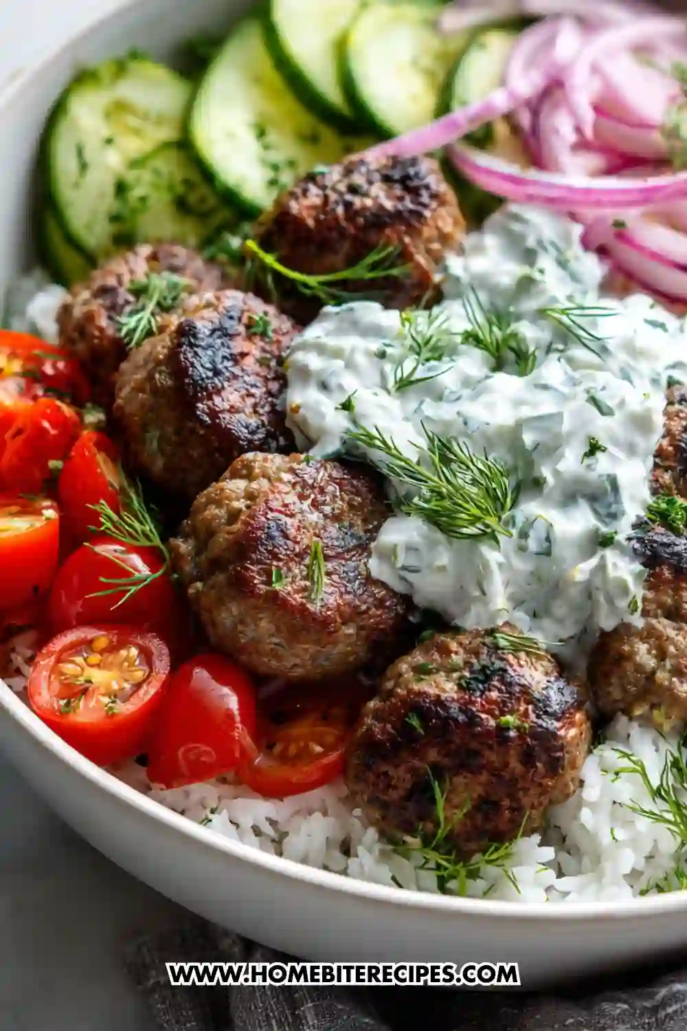A colorful Mediterranean meatball bowl filled with juicy seared meatballs, creamy tzatziki, fresh cherry tomatoes, sliced cucumbers, pickled red onions, and fluffy white rice, garnished with fresh dill.