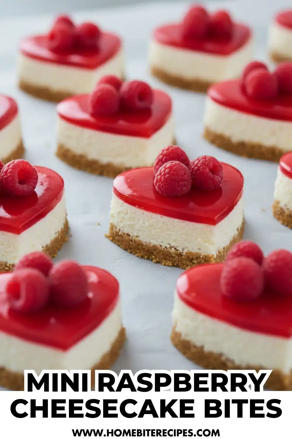 Heart-shaped raspberry cheesecake bites with a biscuit crust, creamy cheesecake layer, glossy raspberry topping, and fresh raspberries on top, arranged on parchment paper.